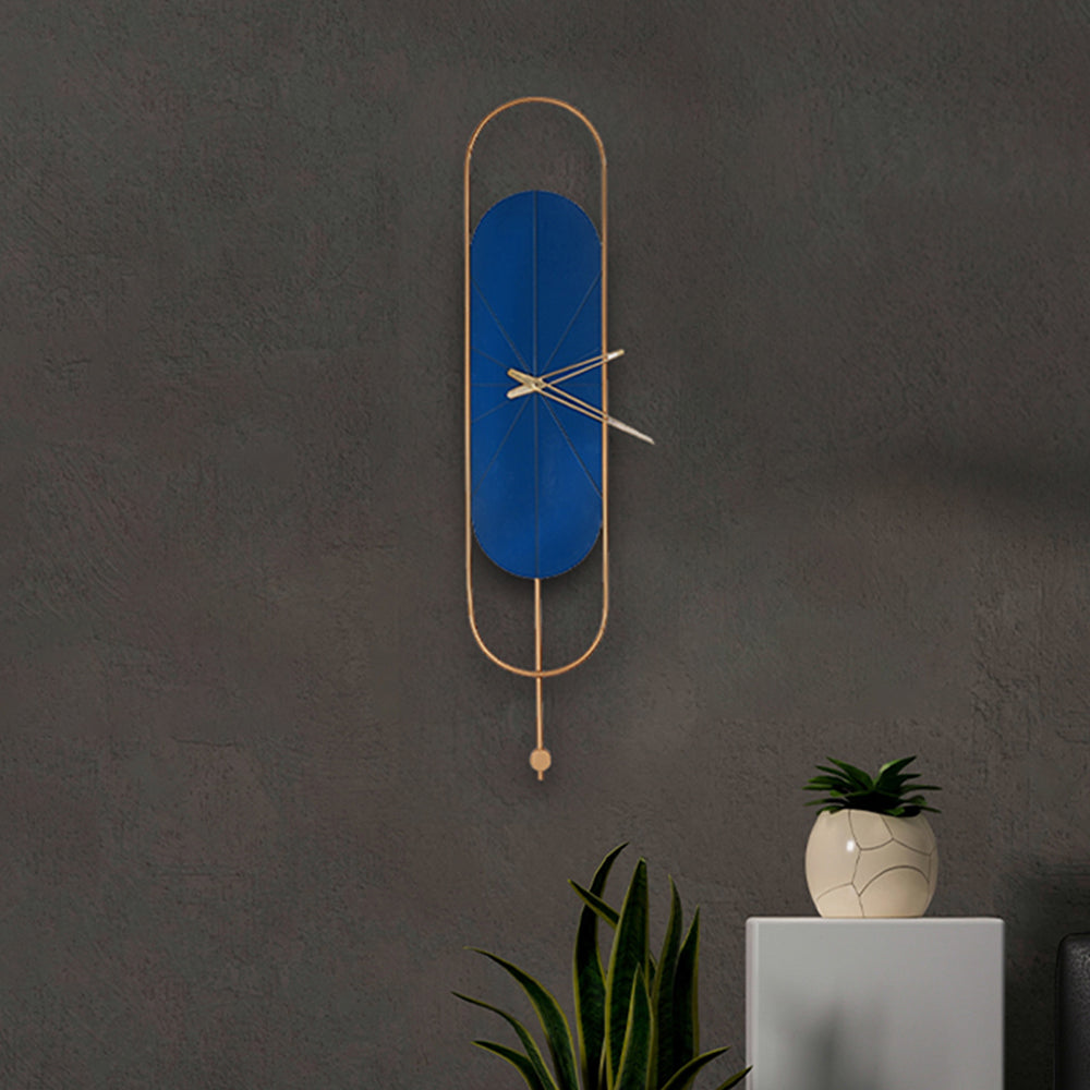 Long blue and golden colored metallic wall clock with pendulum design in a dark themed living room set-up.