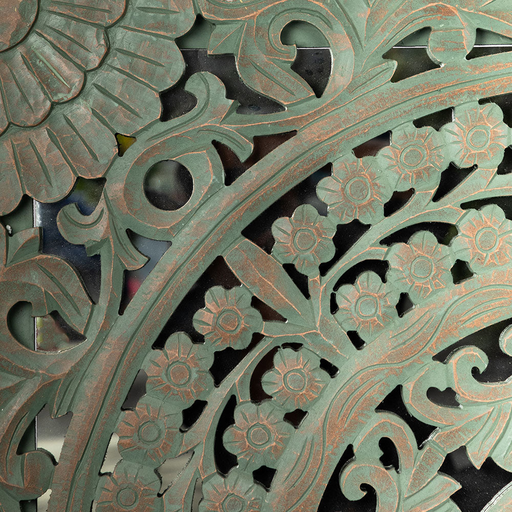 A large square wooden hand-carved wall hanging with a mirror base- close-up view.