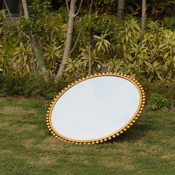 Side view of a large round mirror bordered with metallic small spheres.