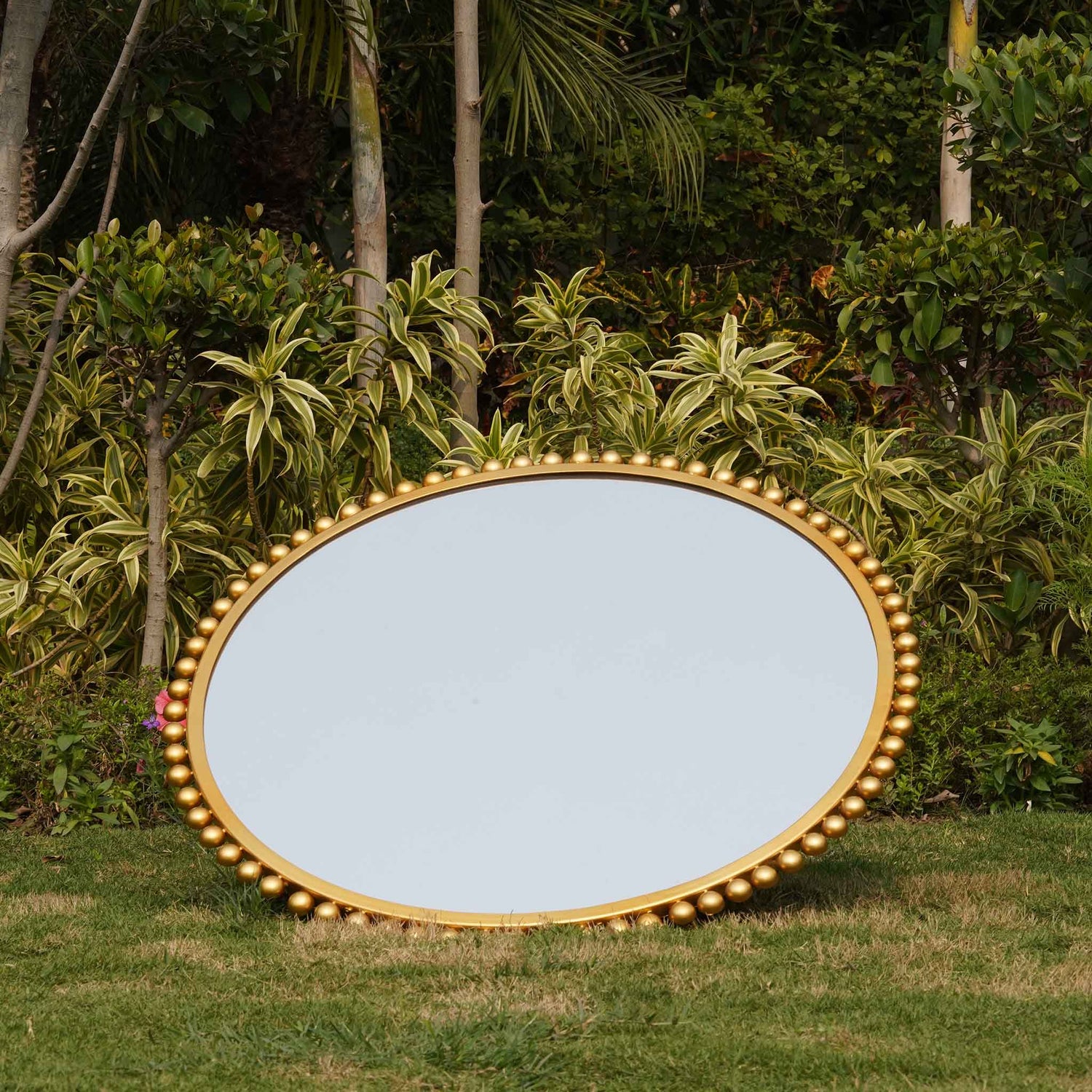 Front view of a large round mirror bordered with metallic small spheres.
