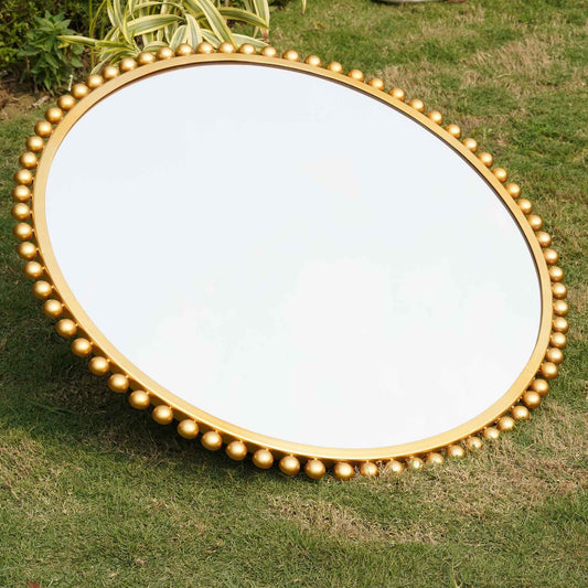 Close side view of a large round mirror bordered with metallic small spheres.