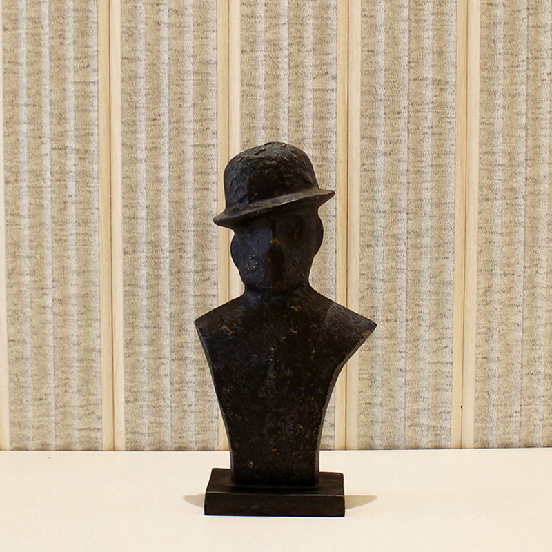 A black metallic table-top sculpture of a man wearing a tilted hat placed on a table.