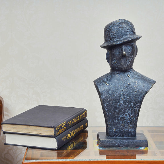 Front view of a black metallic table-top sculpture of a man wearing a tilted hat.