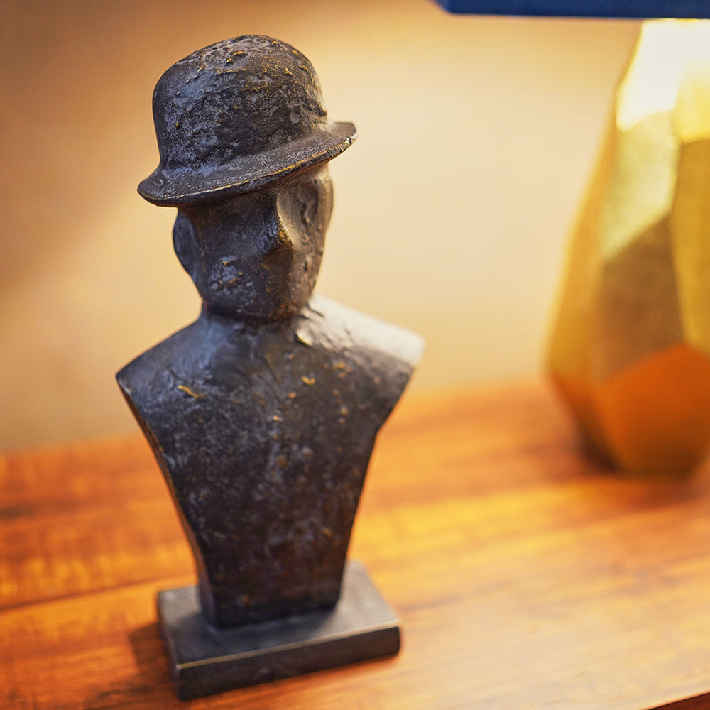 Side view of a black metallic table-top sculpture of a man wearing a tilted hat, placed on a side table. 