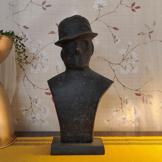 Front view of a black metallic table-top sculpture of a man wearing a tilted hat.