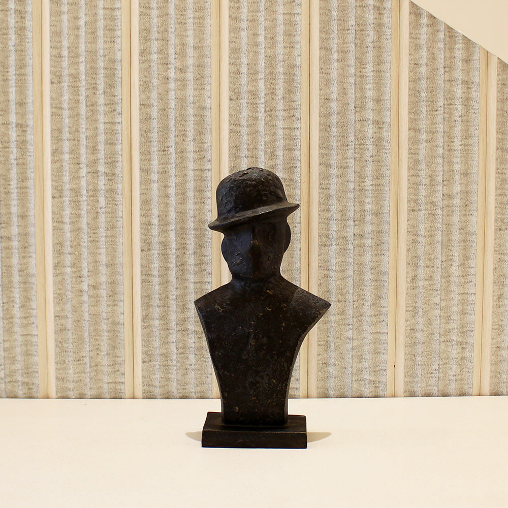 A black metallic table-top sculpture of a man wearing a tilted hat placed on a table.