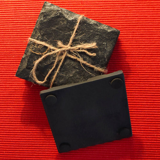 Four square shaped black slate stone coasters placed on a red table runner.