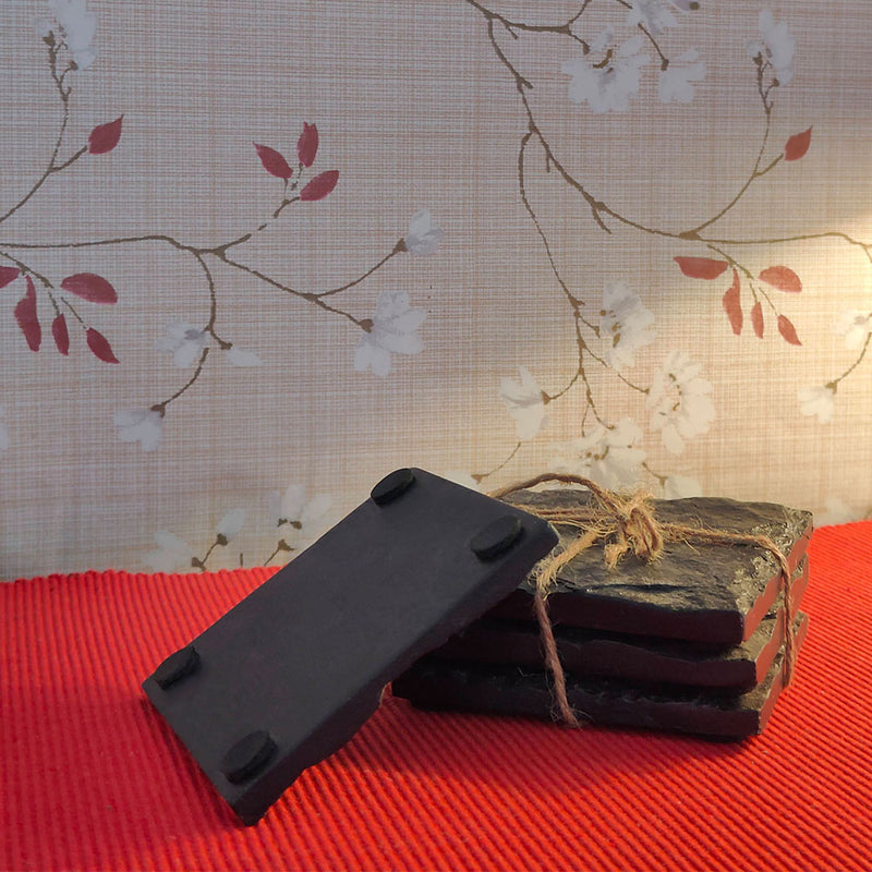 Four square shaped black slate stone coasters placed on a red table runner in a side angle.