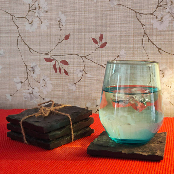 Three square shaped black slate stone coasters placed on  each other and one coaster on the side with a glass kept on top.