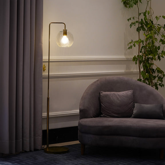 A golden sleek metallic floor lamp with a round globe glass as its head is placed in a living room.