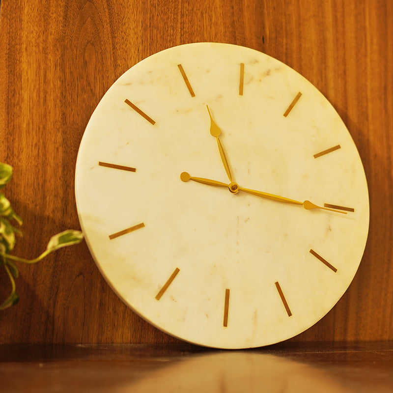 Side view of a large and heavy white marble clock with brass inlay placed on a console table.