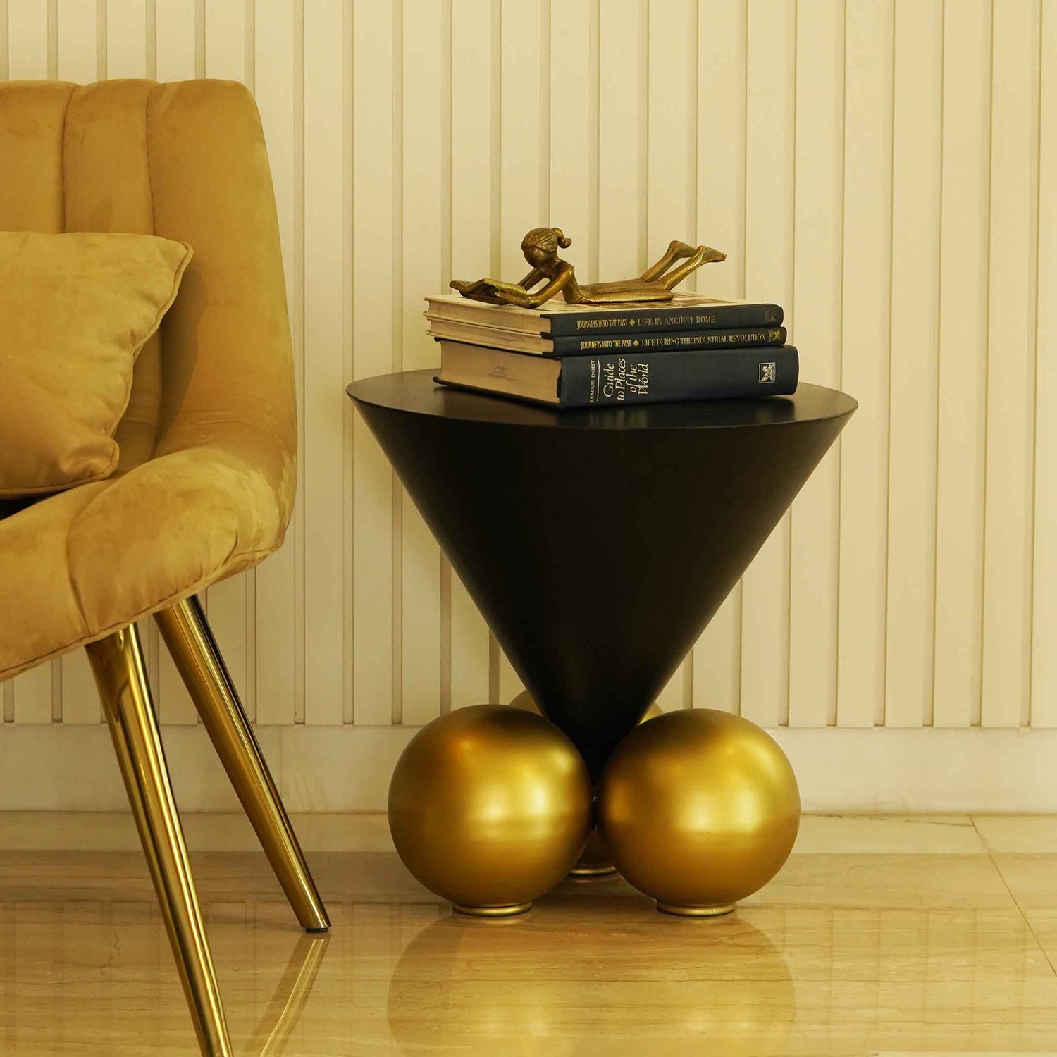Modern design black inverted cone table with 3 spherical golden balls on the base. placed next to a chair.