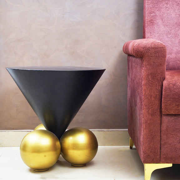 Modern design black inverted cone table with 3 spherical golden balls placed on the floor of a living room next to a sofa.