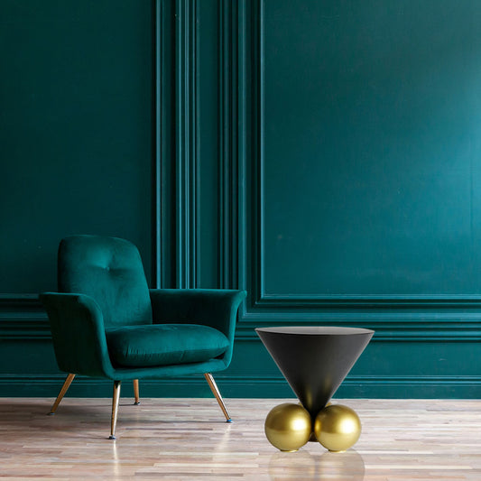 Modern design black inverted cone table with 3 spherical golden balls placed on the floor of a living room next to a blue chair and blue walls.