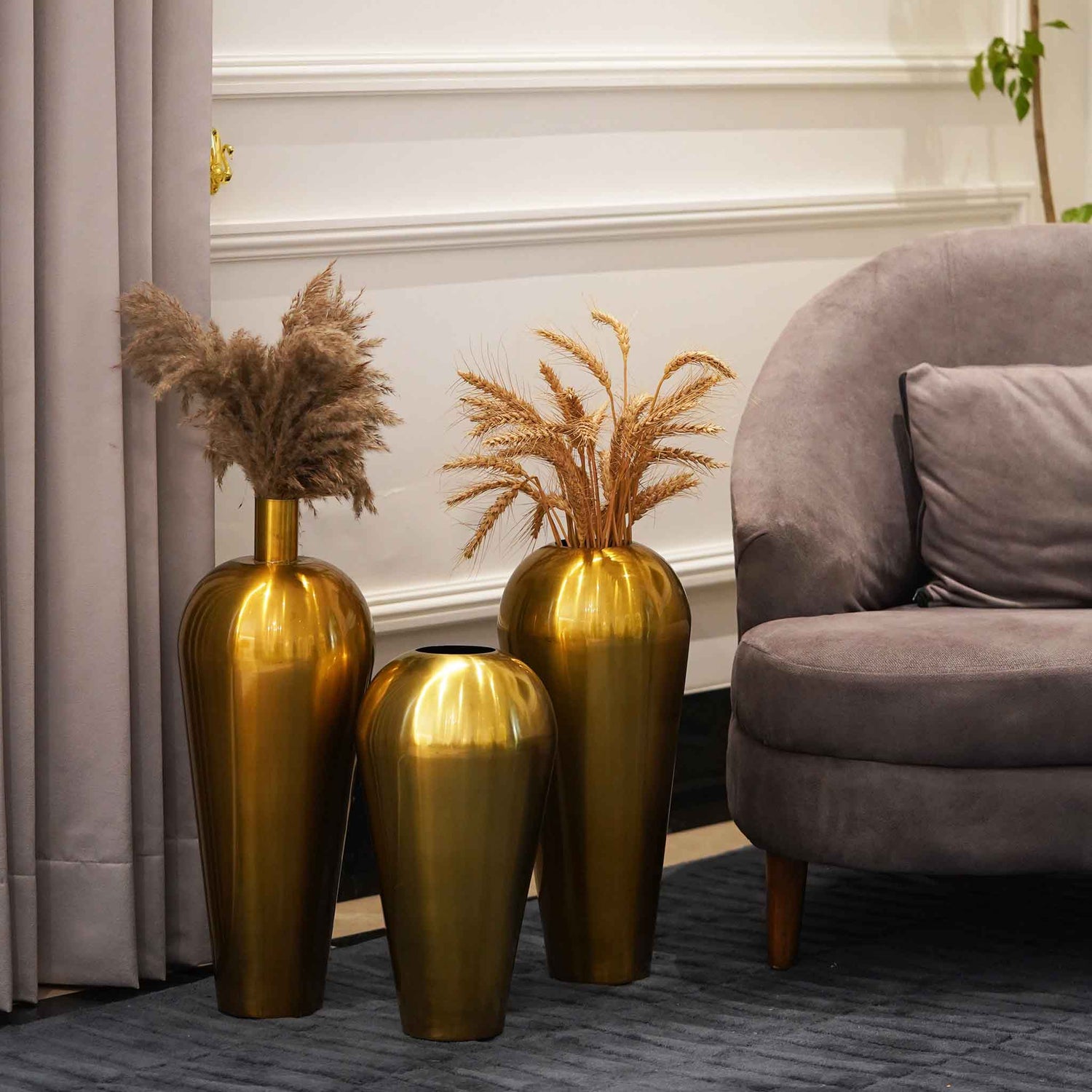 Three tall golden metallic vases placed on the floor of a living room.