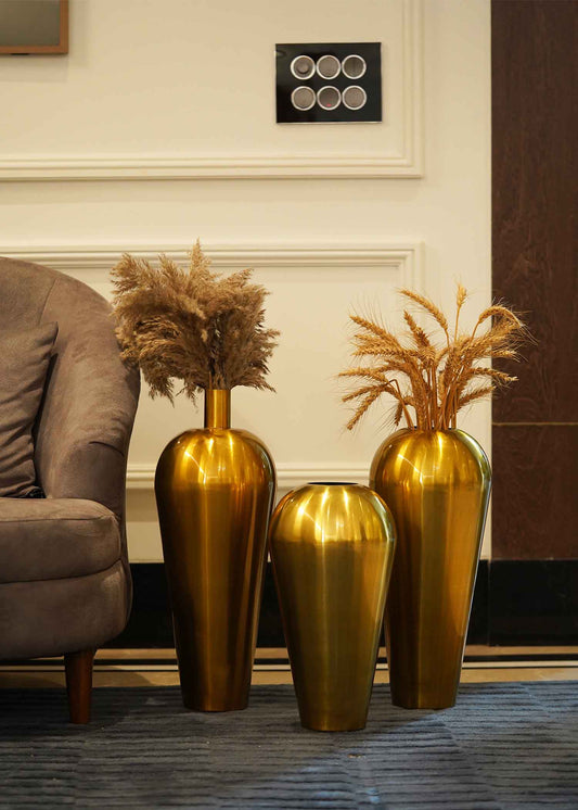 Image of three tall golden metallic vases placed on the floor of a living room.
