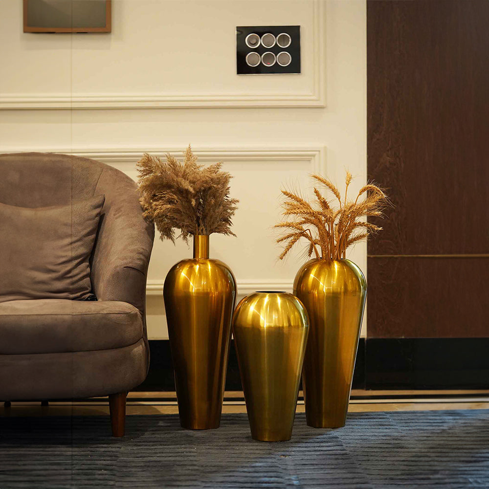 Image of three tall golden metallic vases placed on the floor of a living room.