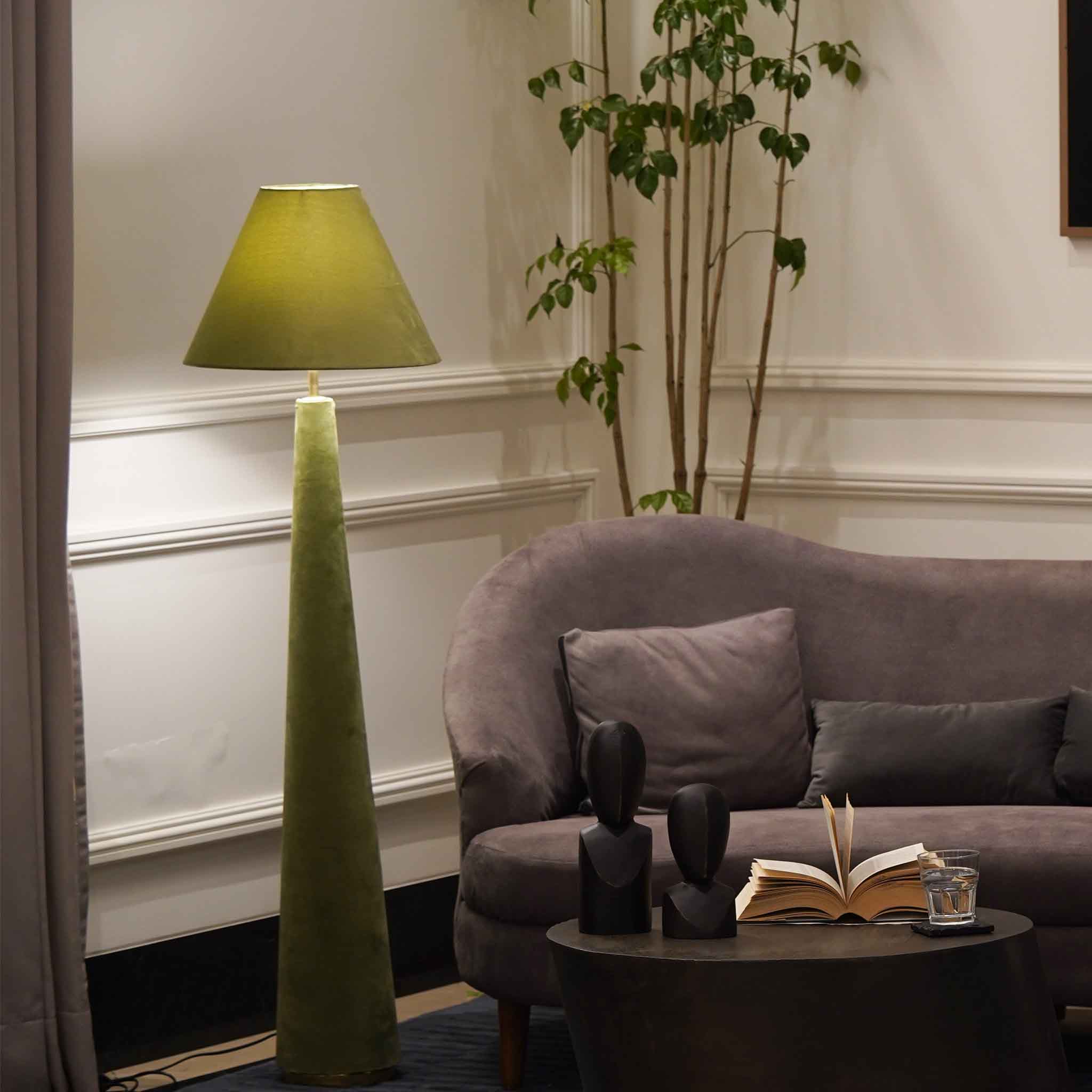 Green colored velvet floor lamp is lit-up and placed in a living room set-up.