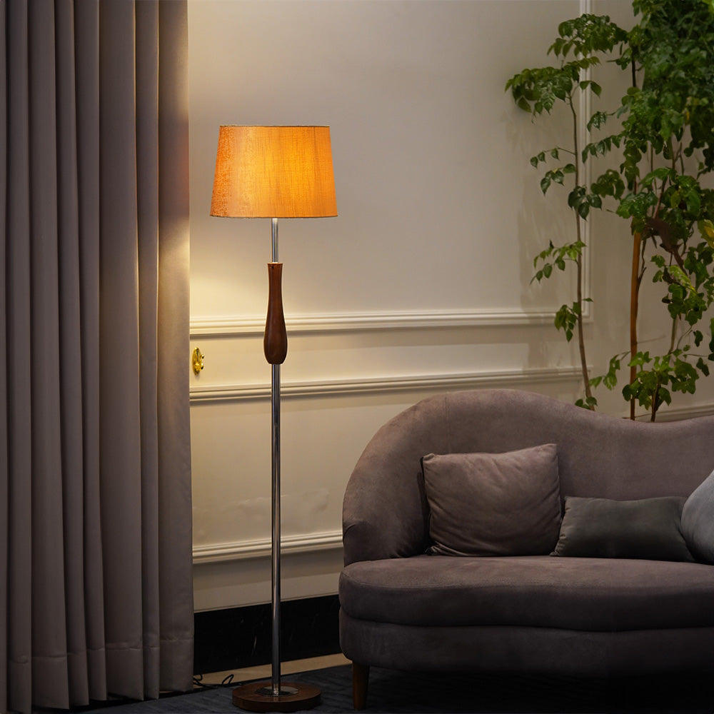 Tall floor lamp in metal and wood is lit-up with a yellow lampshade in a living room.