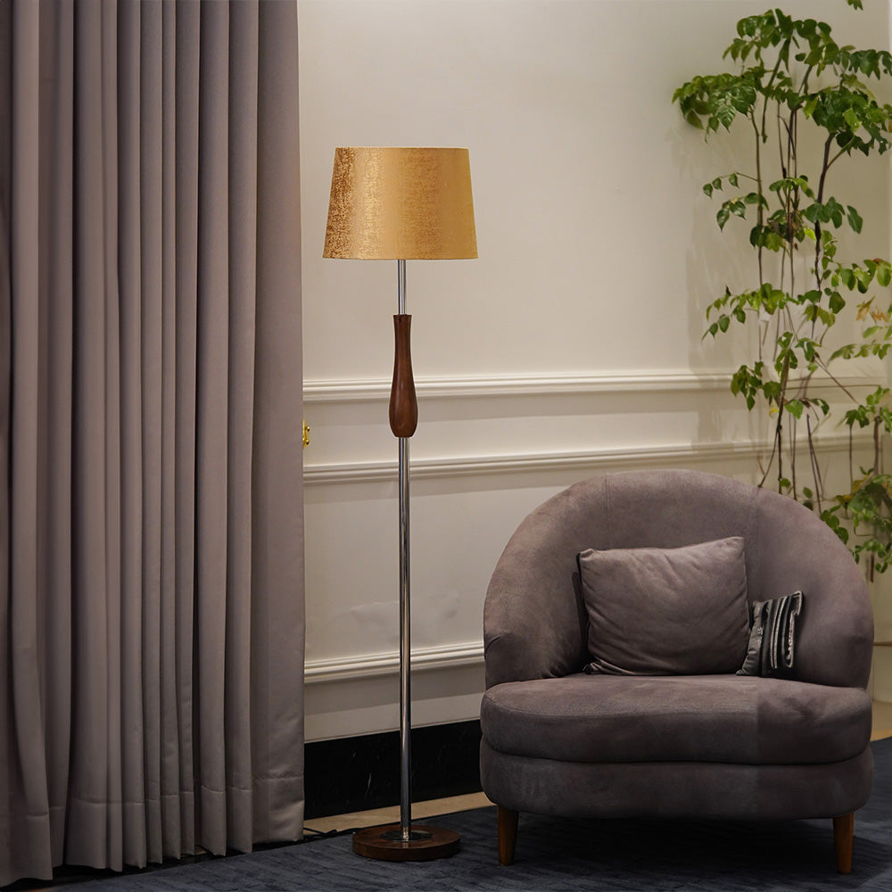 Tall floor lamp in metal and wood with a golden-yellow lampshade in a living room.